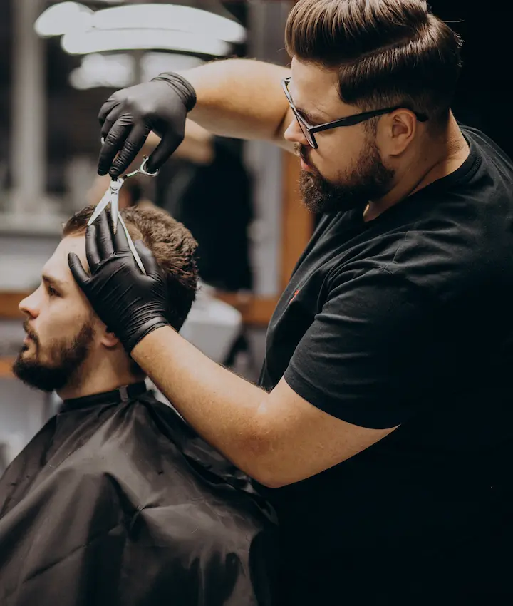 Barber wearing gloves cutting a client's hair with scissors in a barbershop.